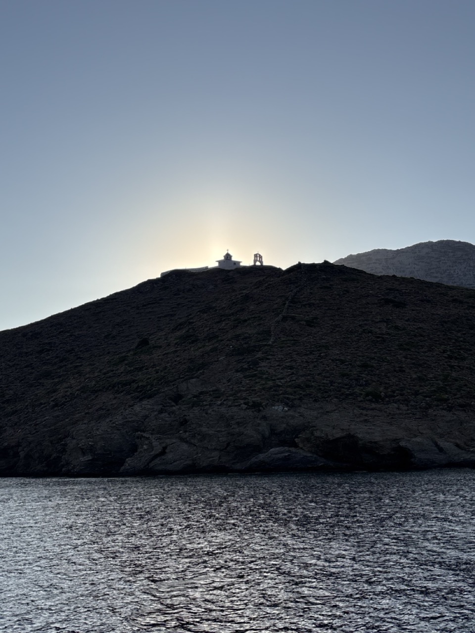 The sun setting exactly behind a whitewashed chapel on a hilltop