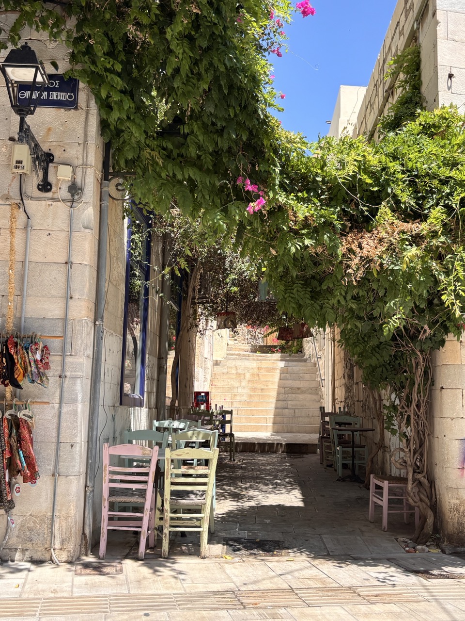 A shaded alley in Ermoupoli — pastel taverna chairs under the bougainvillea